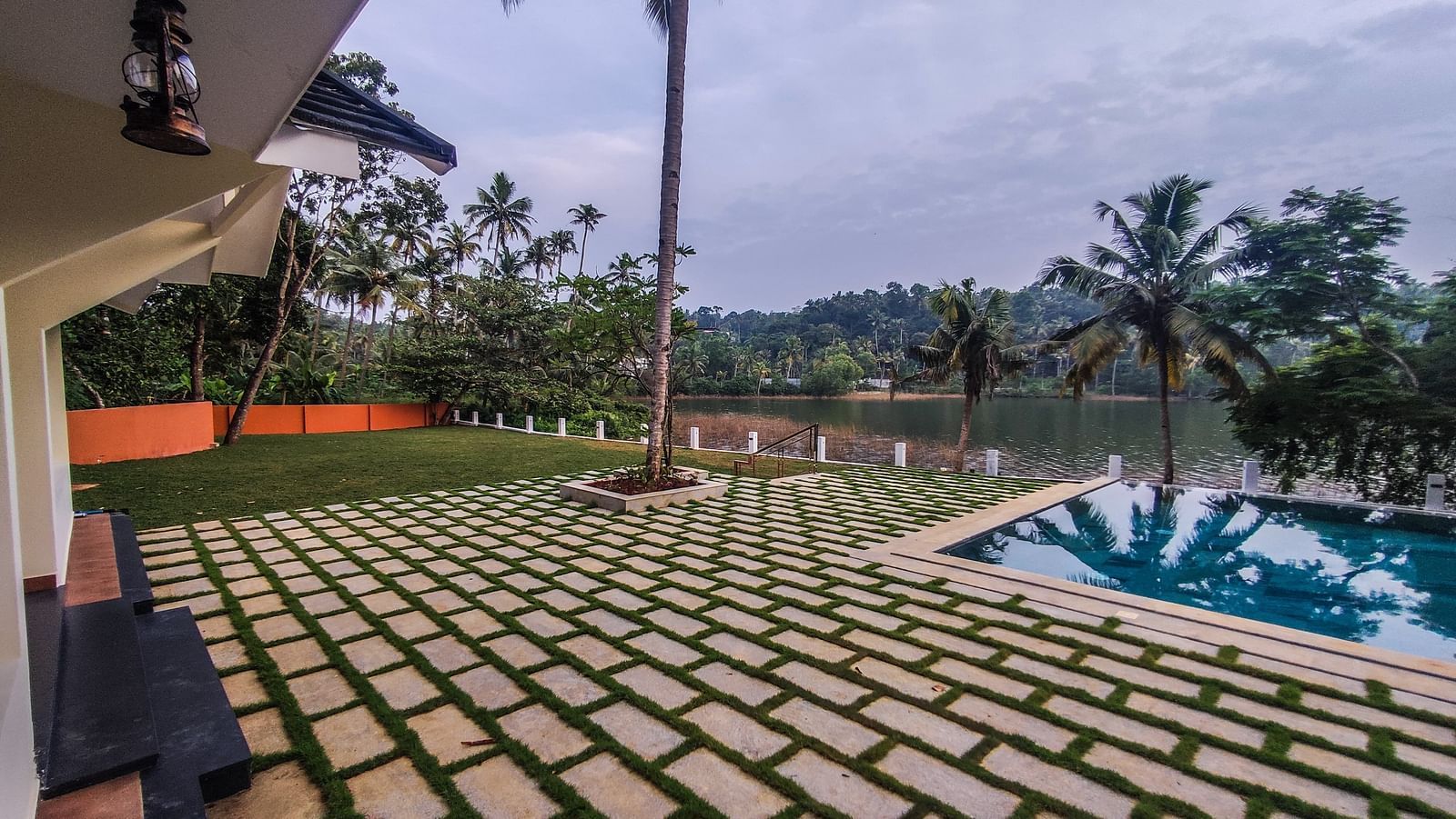 An image of a lawn with grass and stone slabs, and a swimming pool and the entire area is surrounded by trees - Fragnant Nature Kollam